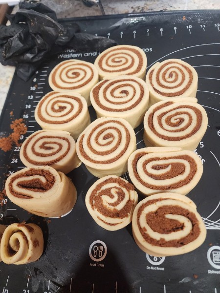 Cinnamon roll dough sliced into spirals on the bench, lined up and ready for the pan.